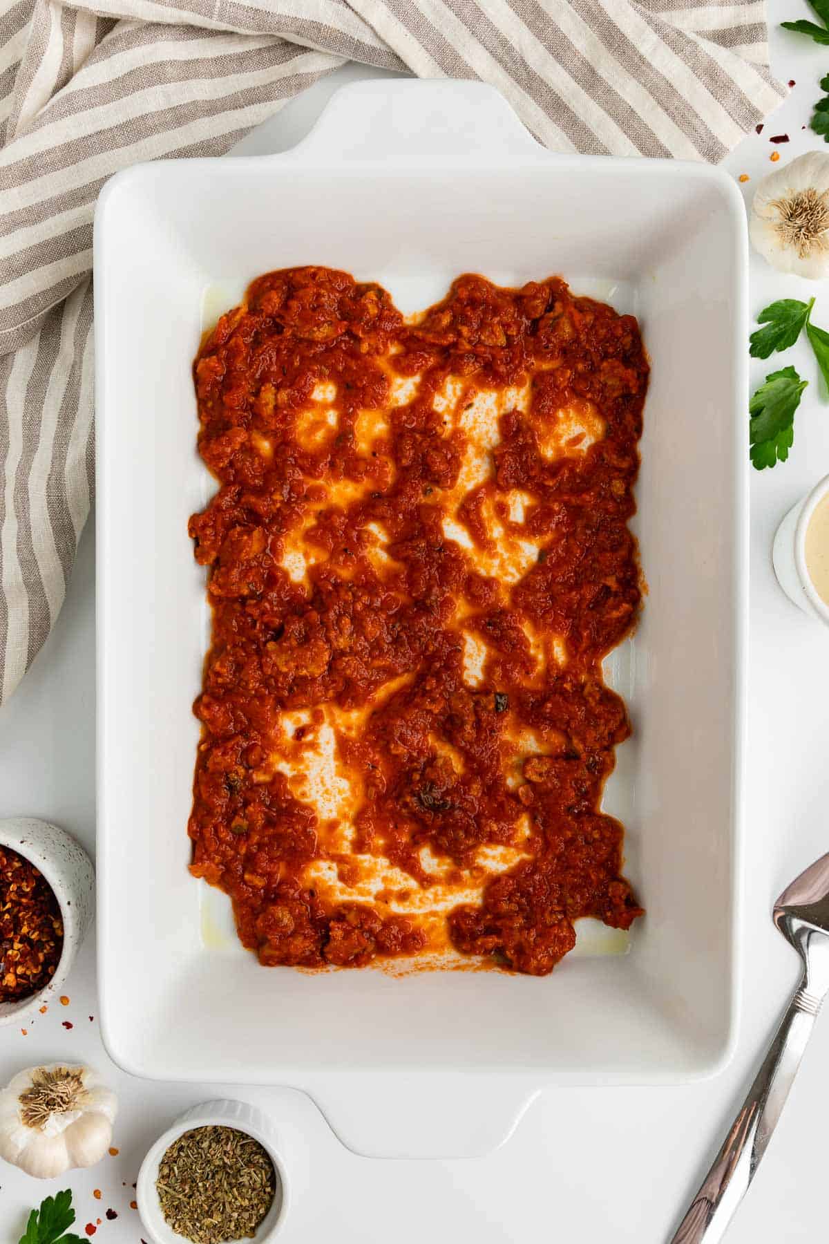 a white casserole dish with marinara sauce spread across the bottom of it