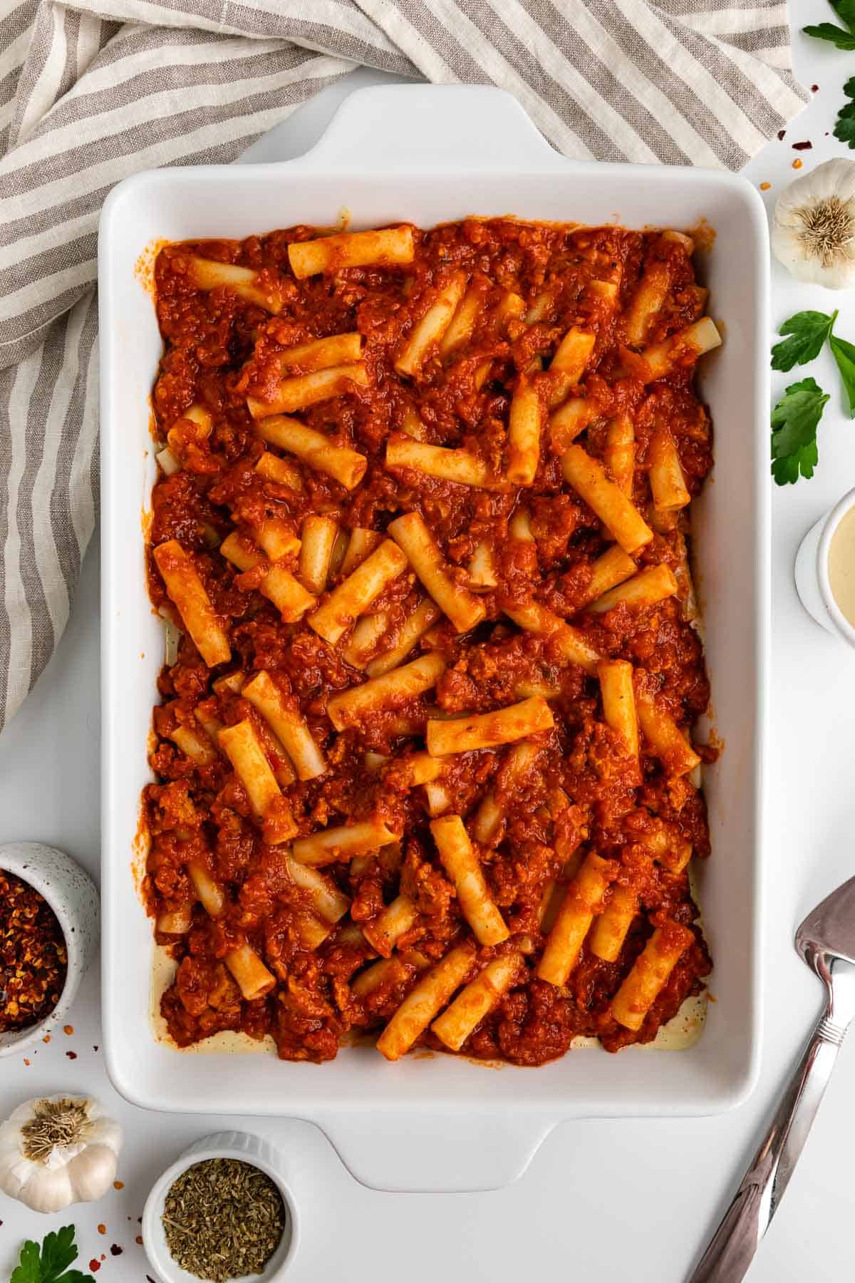 ziti pasta and marinara sauce mixed together inside a white casserole dish