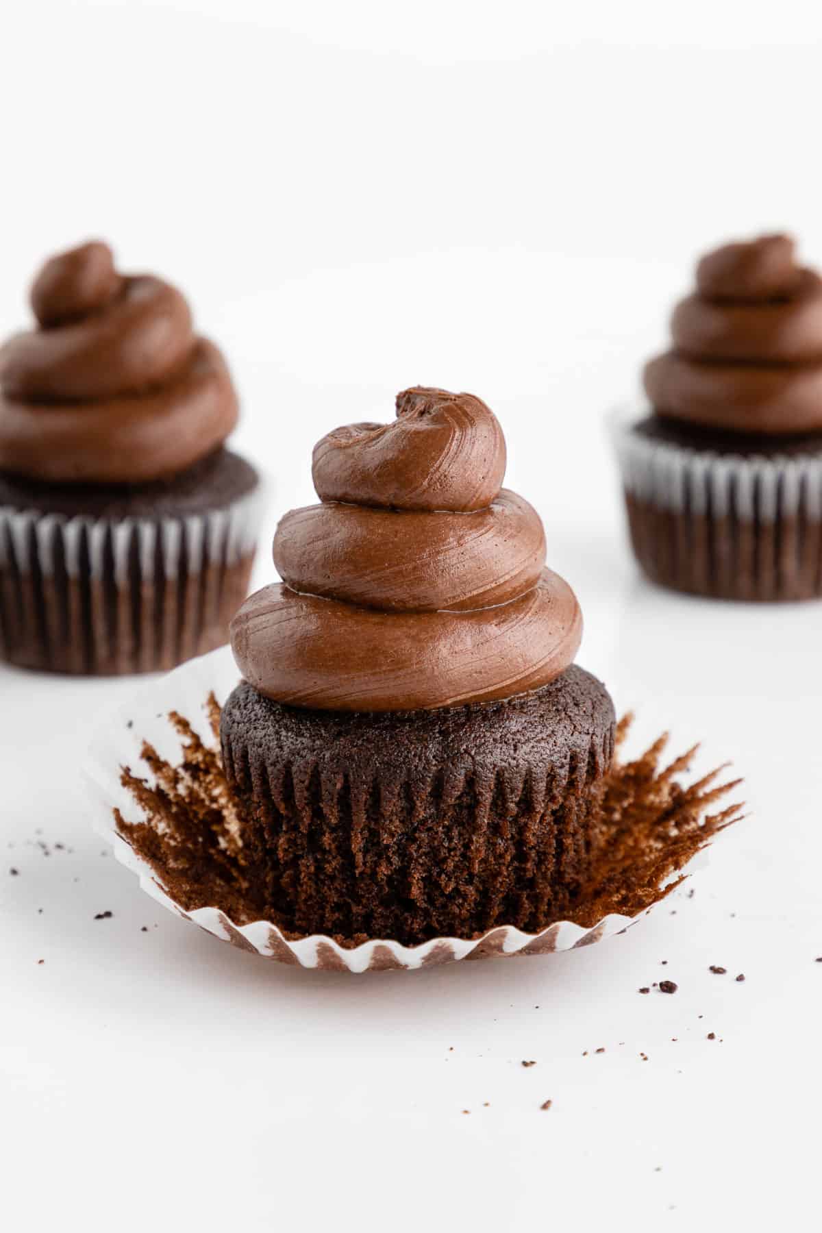 three vegan chocolate cupcakes with the cupcake liner partially peeled off the middle cupcake