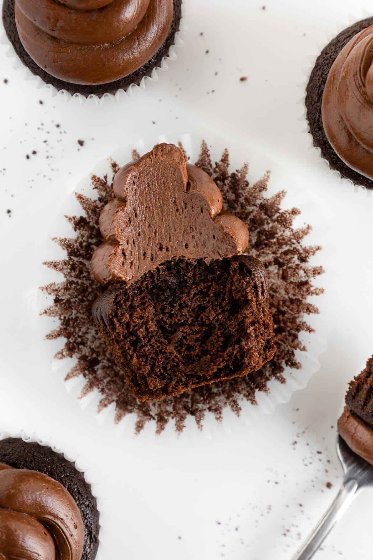 a vegan chocolate cupcake cut in half laying on top of a parchment paper cupcake liner