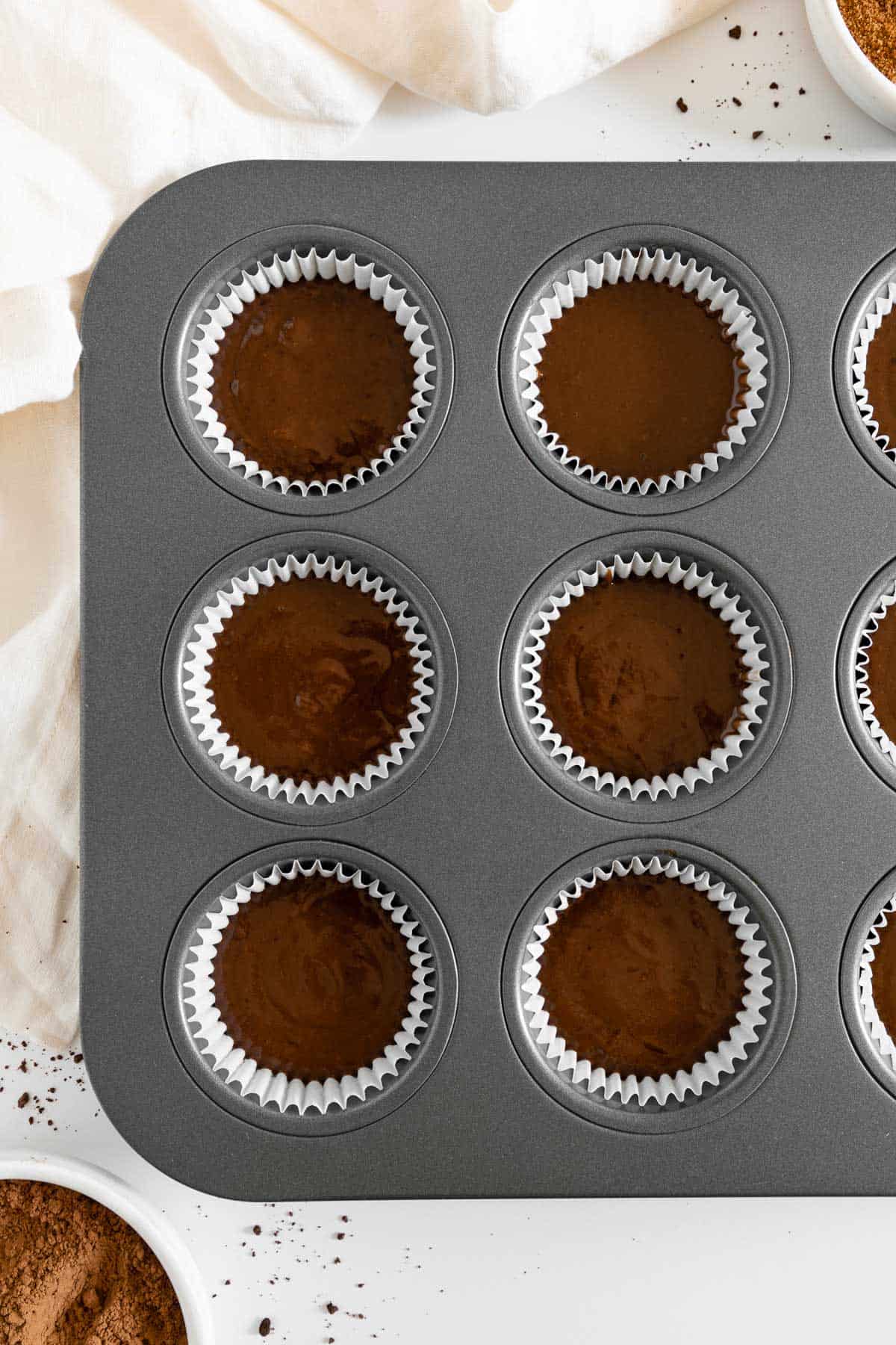 a muffin tin filled with cupcake liners and chocolate cake batter inside them