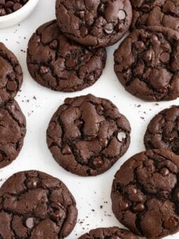 a dozen vegan double chocolate chip cookies laying on white parchment paper