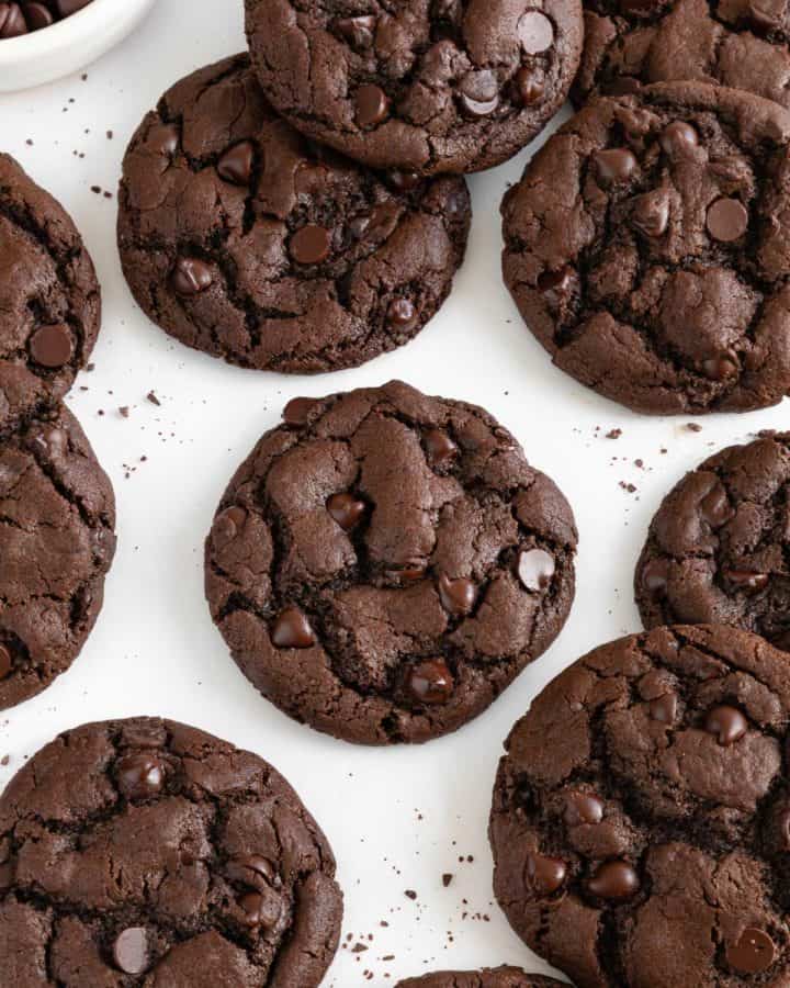 a dozen vegan double chocolate chip cookies laying on white parchment paper