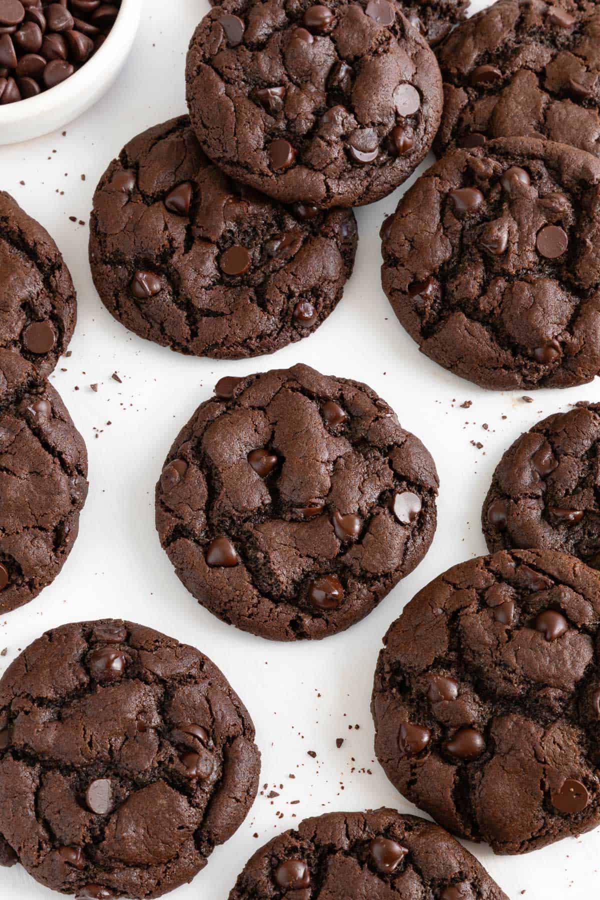 a dozen vegan double chocolate chip cookies laying on white parchment paper