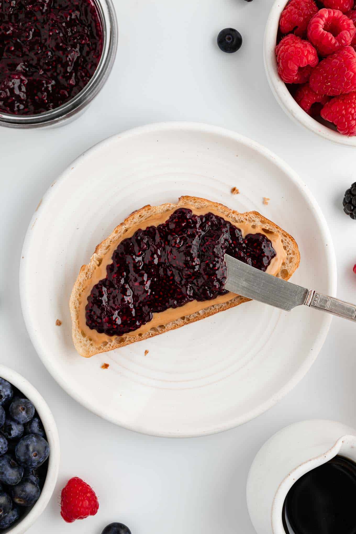 a knife spreading berry chia jam on peanut butter toast on a white plate