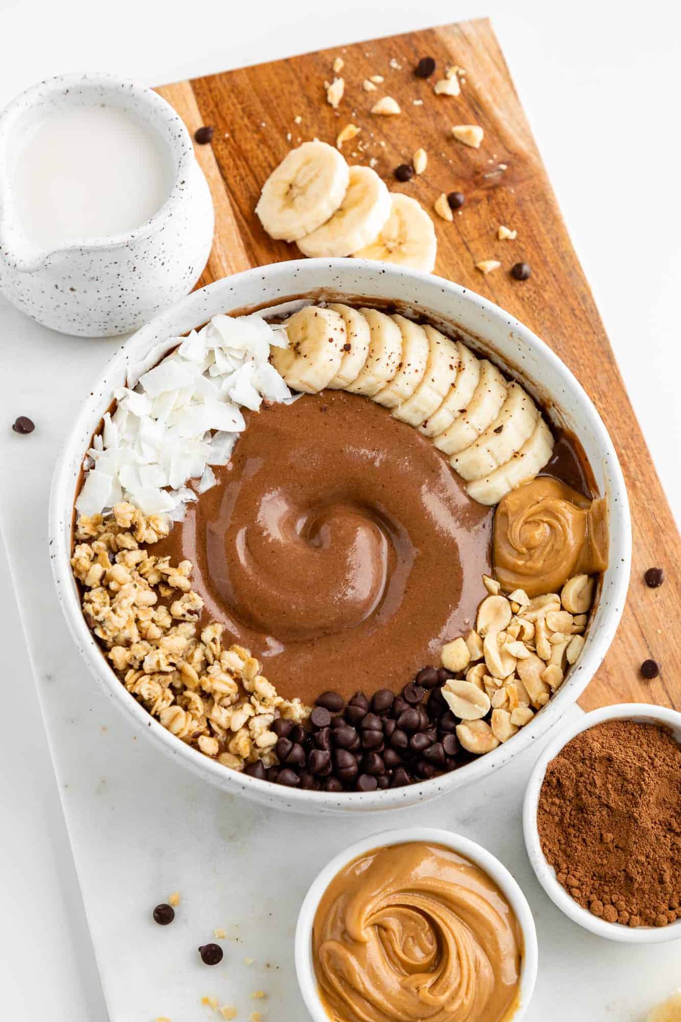 a close up image of a vegan peanut butter chocolate smoothie bowl topped with banana and coconut flakes