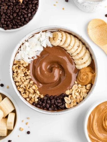 chocolate peanut butter smoothie bowl surrounded by bowls of ingredients, including banana, chocolate chips, and almond milk