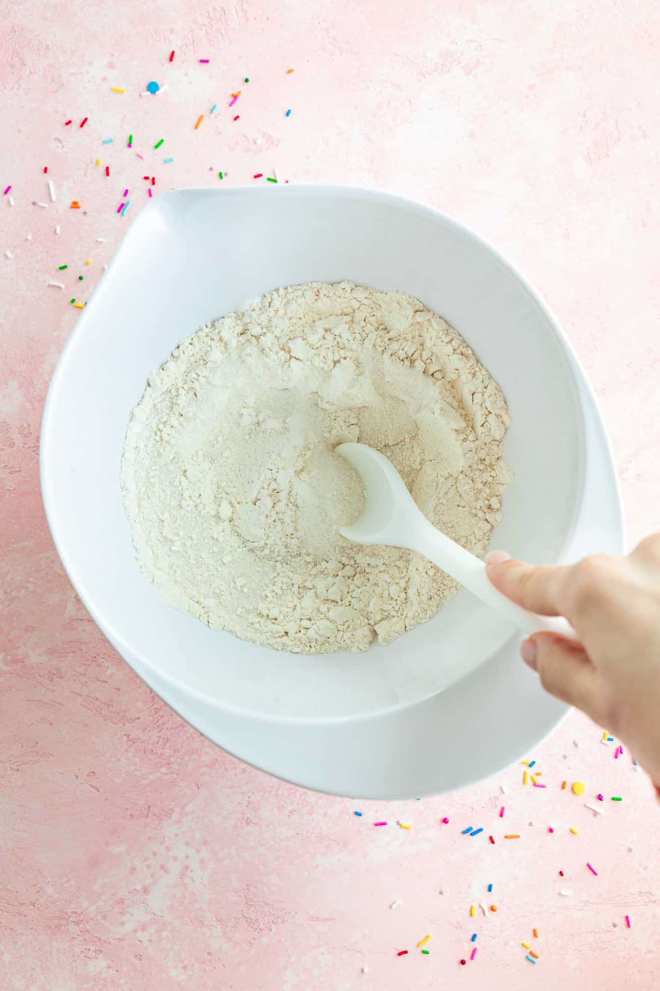 a hand mixing flour and sugar in a white bowl