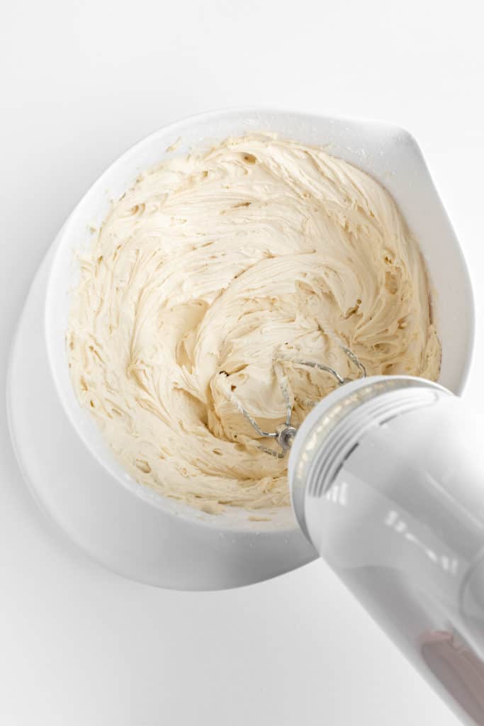 a handheld electric mixer creaming vegan vanilla frosting in a white mixing bowl