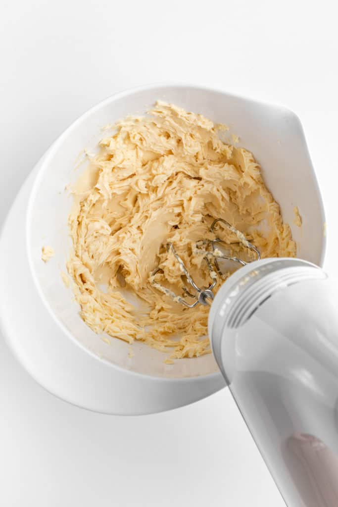 a hand electric mixer creaming vegan butter in a white mixing bowl