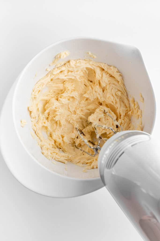 a handheld electric mixer creaming vegan butter in a white mixing bowl