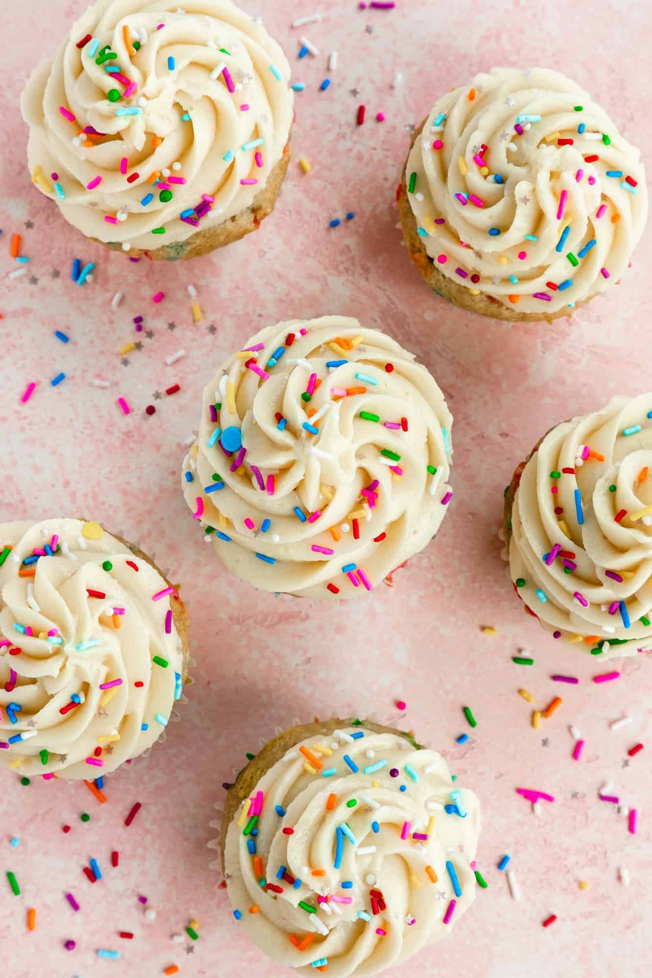 an overhead image of vegan cupcakes with vanilla buttercream frosting and rainbow sprinkles 