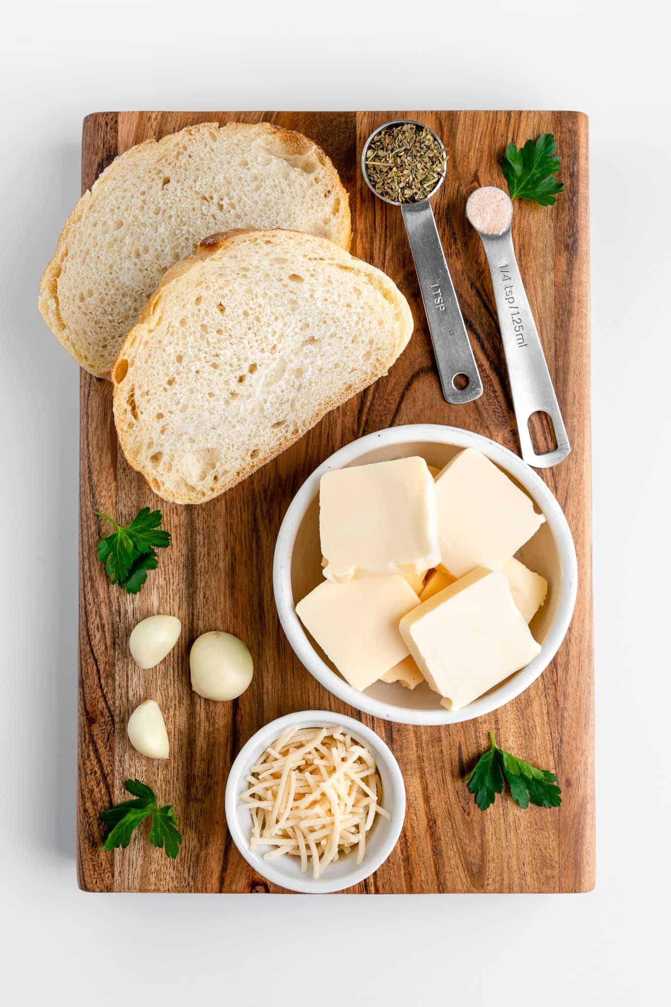 wood board topped with sourdough bread, vegan butter, parsley, italian seasoning, garlic cloves, and salt
