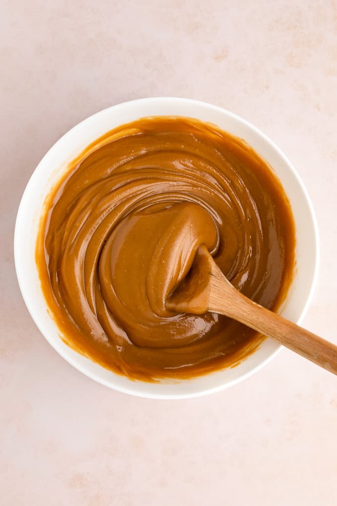 a wooden spoon mixing healthy vegan peanut butter caramel in a white bowl