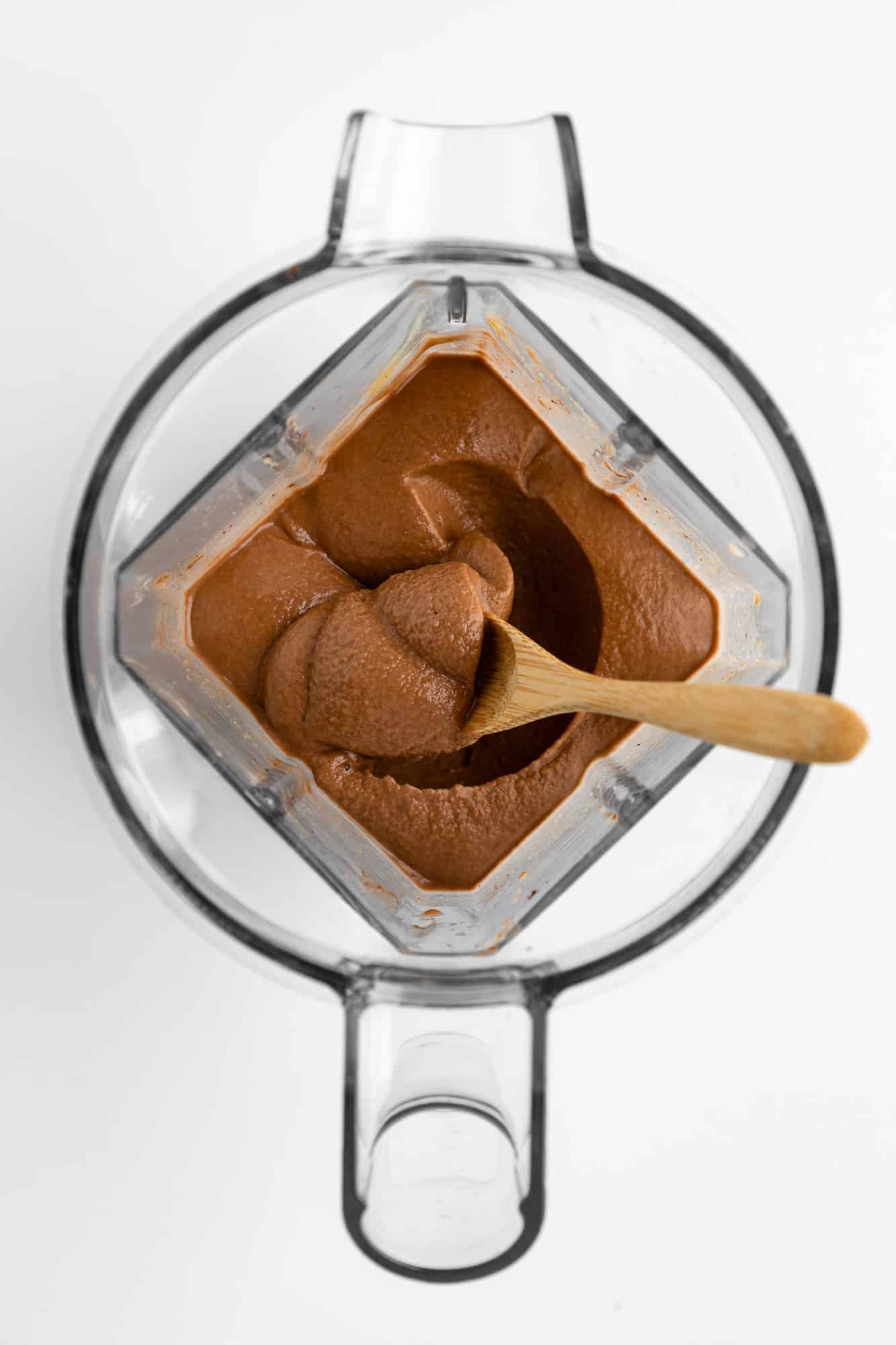 a wooden spoon scooping thick chocolate smoothie out of a vitamix blender