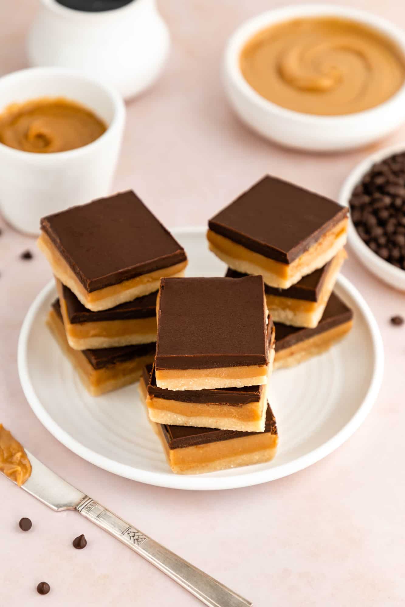 three stacks of no-bake vegan millionaire shortbread bars on a white plate surrounded by ingredients