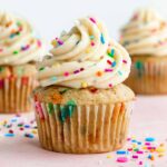 three vegan funfetti cupcakes with vanilla buttercream frosting and rainbow sprinkles