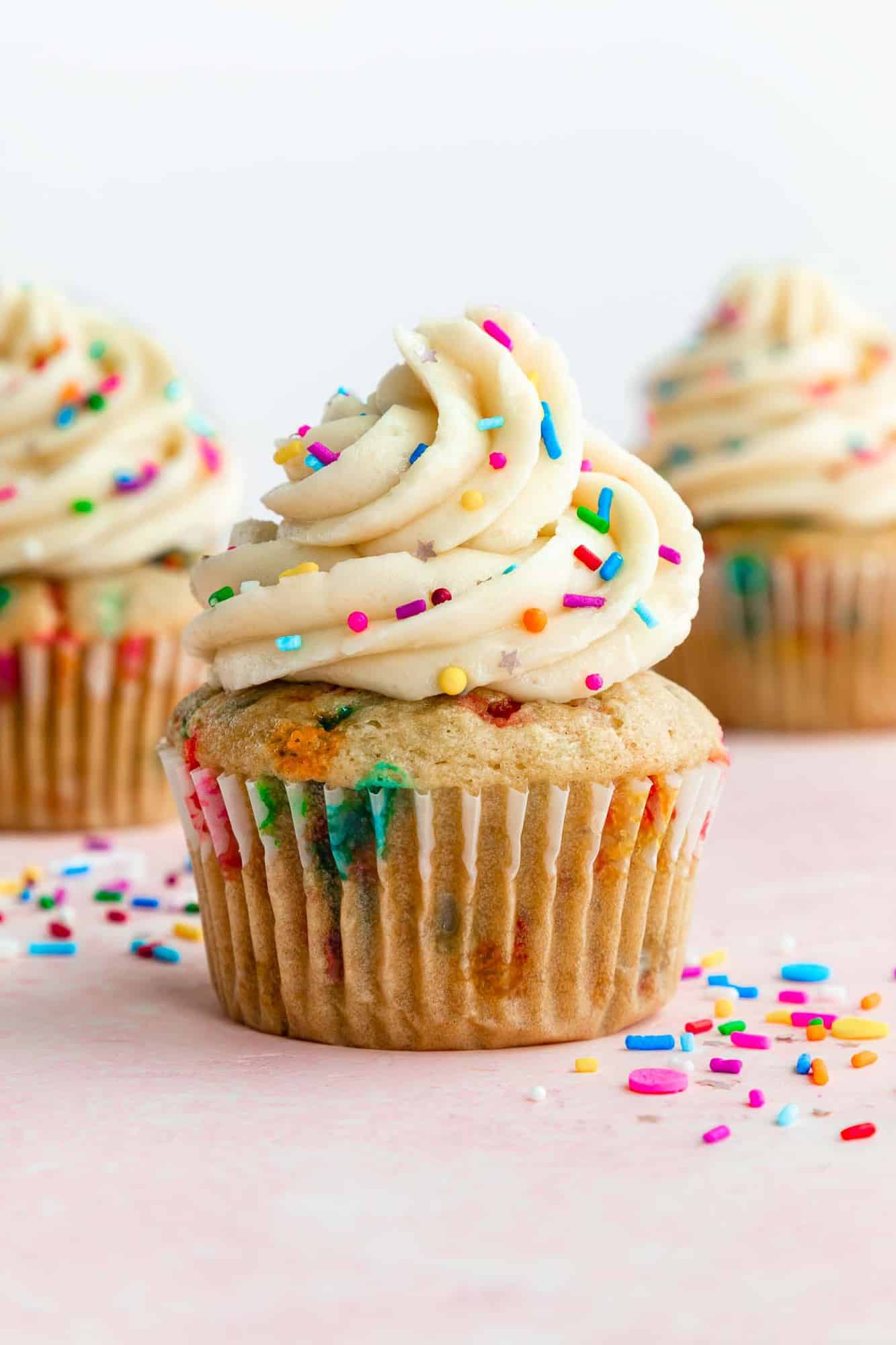 three vegan funfetti cupcakes with vanilla buttercream frosting and rainbow sprinkles