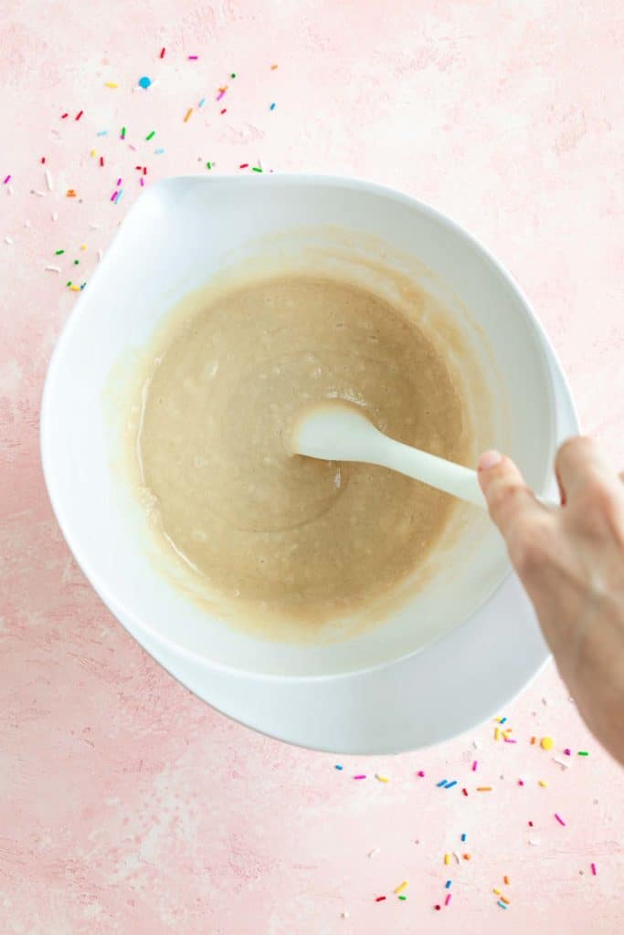 a hand mixing vegan cake batter in a white bowl