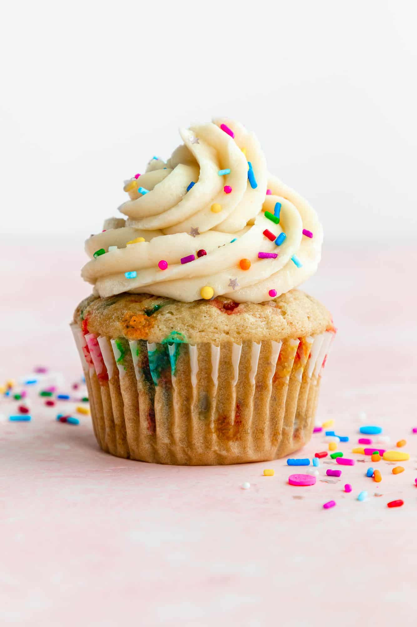 a vegan funfetti cupcake topped with vanilla buttercream frosting and rainbow sprinkles