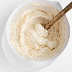 a wooden spoon mixing vegan vanilla frosting in a white mixing bowl