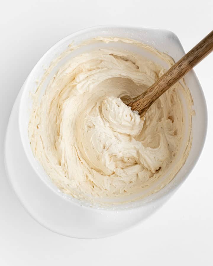 a wooden spoon mixing vegan vanilla frosting in a white mixing bowl