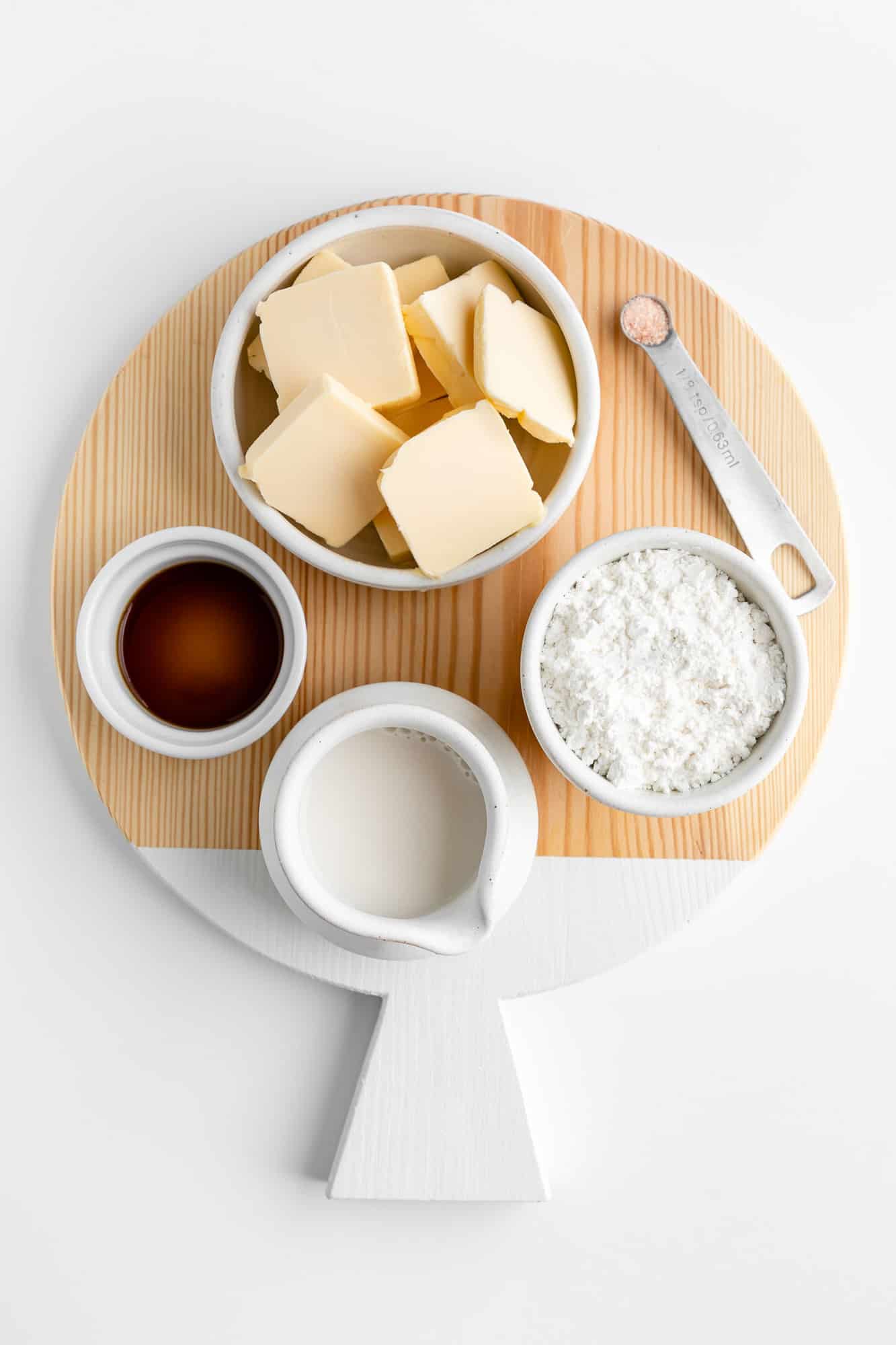 a round wood serving board topped with bowls of vegan butter, powdered sugar, vanilla extract, almond milk, and salt