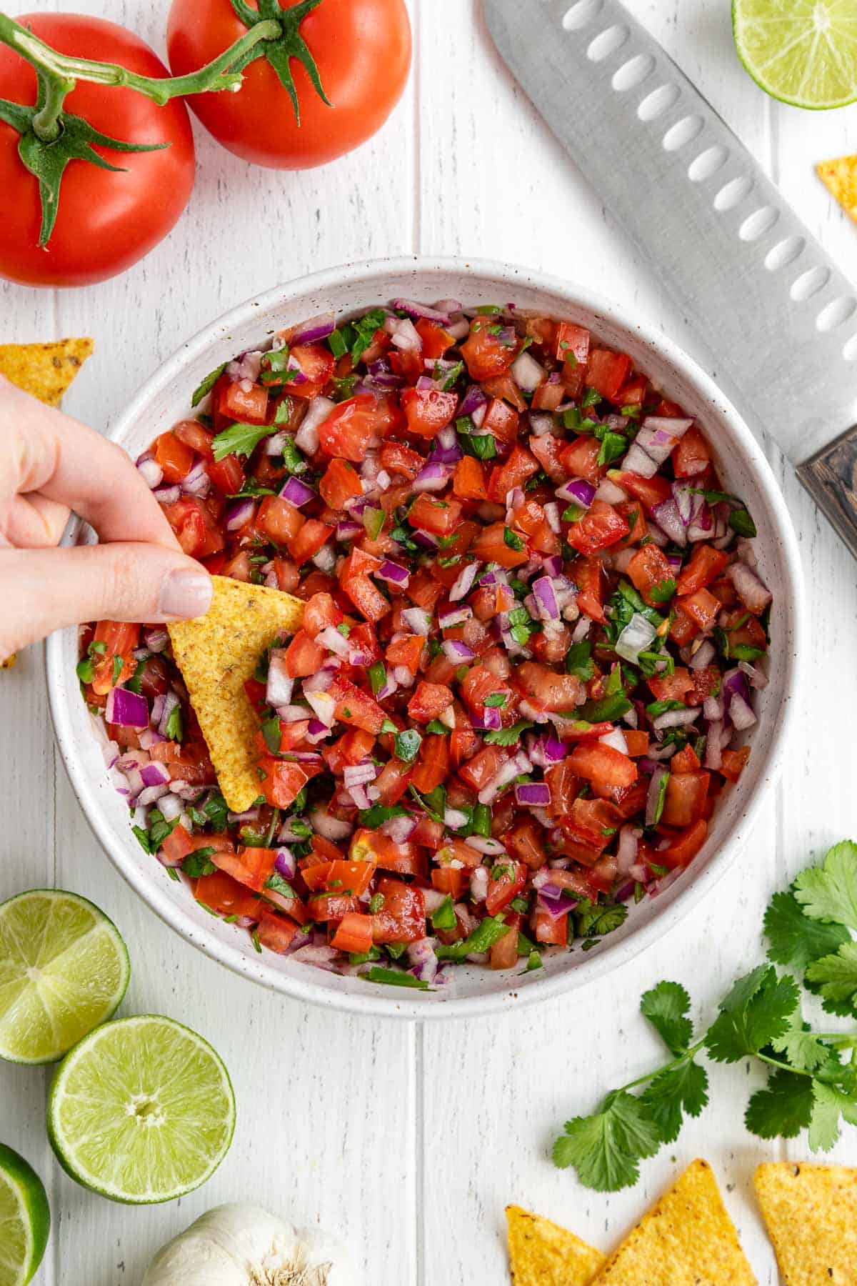 a hand scooping pico de gallo with a tortilla chip