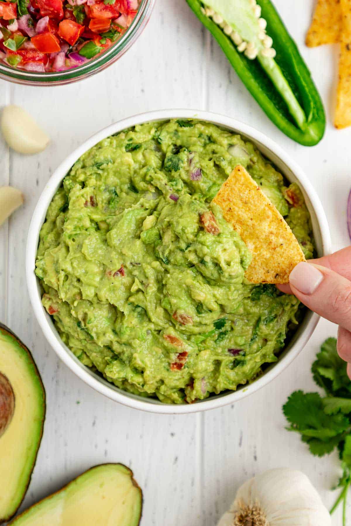 a tortilla chip scooping guacamole out of a white bowl
