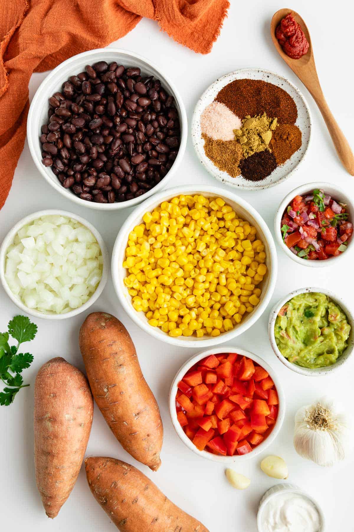 bowls of black beans, corn, onion, red peppers, spices, guacamole, pico de gallo, and three sweet potatoes