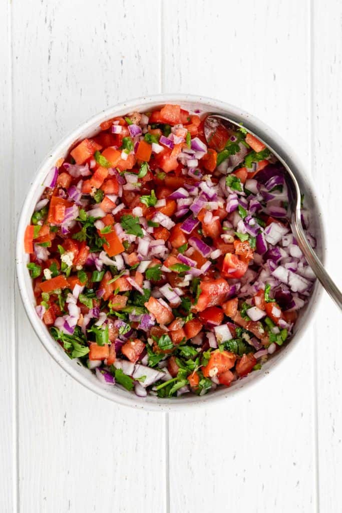 mixing pico de gallo in a white speckled bowl with a large spoon