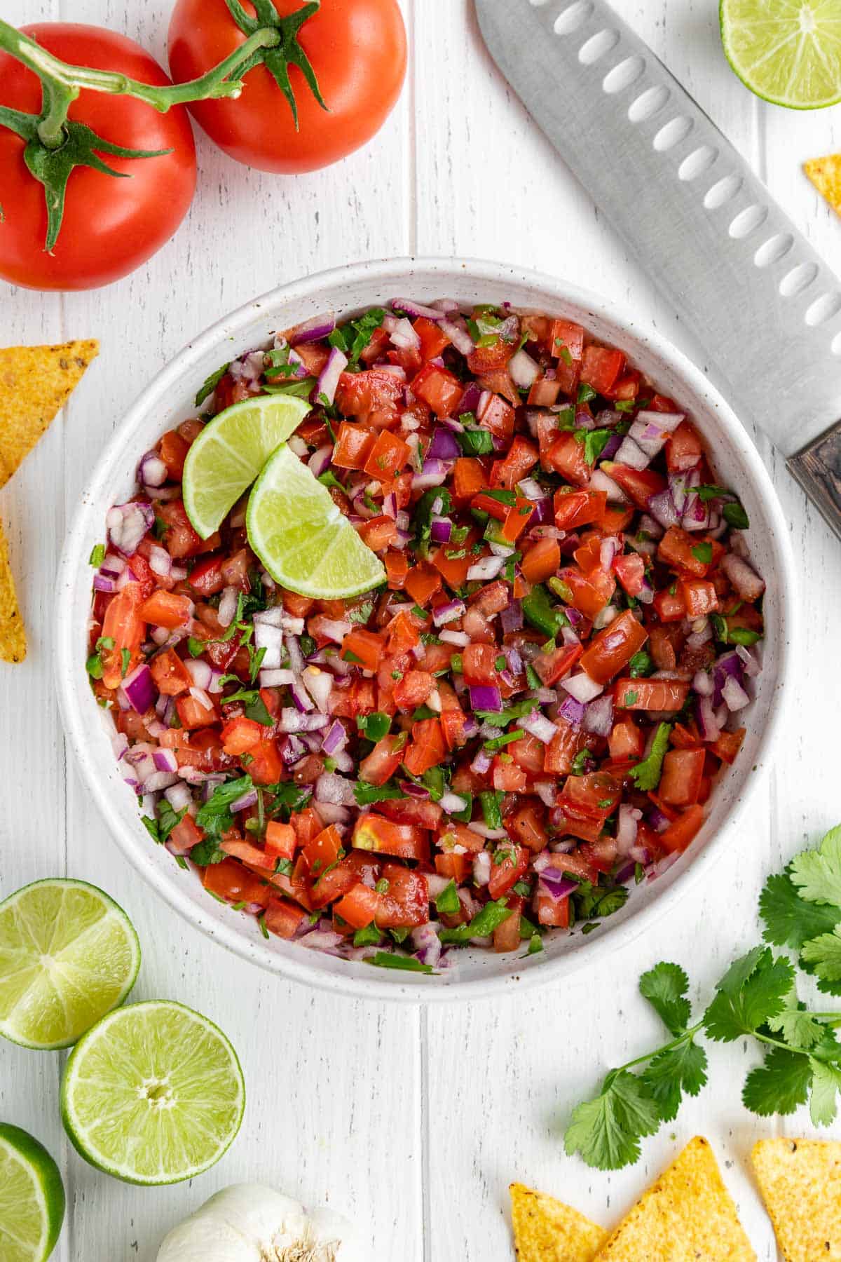 pico de gallo inside a white speckled bowl with lime wedges, surrounded by ingredients