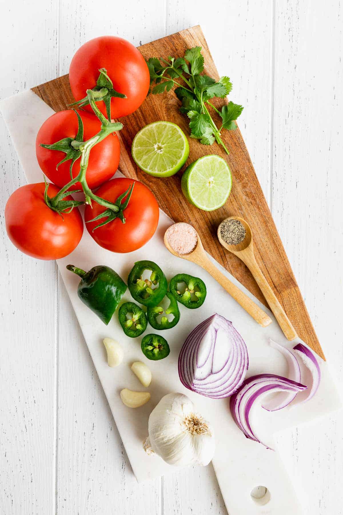 tomatoes, limes, red onion, cilantro, garlic, and jalapeño on a wood and marble serving board