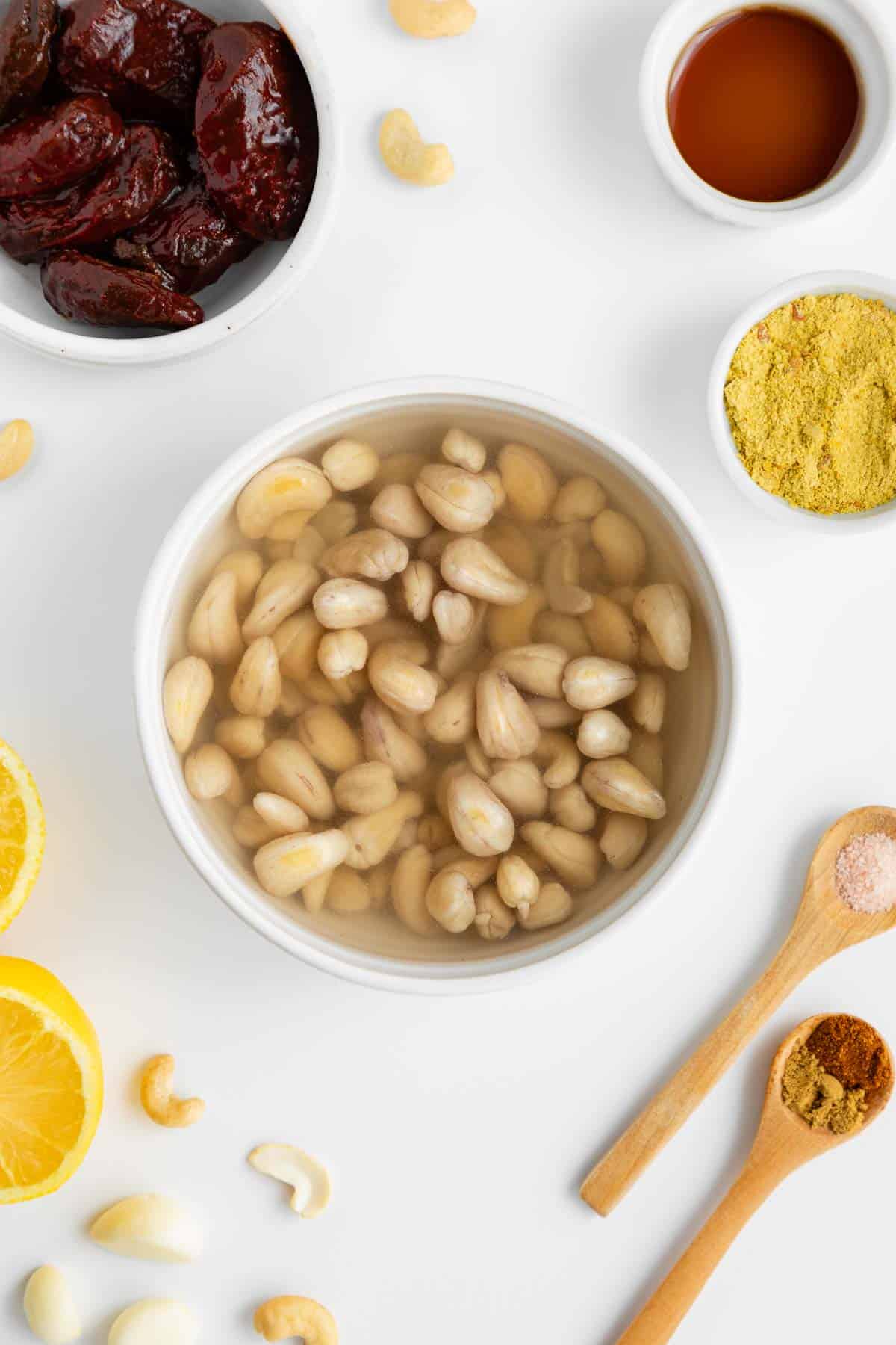 raw cashews soaking in water inside a white bowl surrounded by ingredients for vegan chipotle aioli