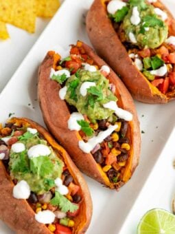 three mexican stuffed sweet potatoes with black beans, corn, guacamole, pico de gallo, and vegan sour cream