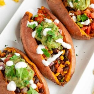 three mexican stuffed sweet potatoes with black beans, corn, guacamole, pico de gallo, and vegan sour cream