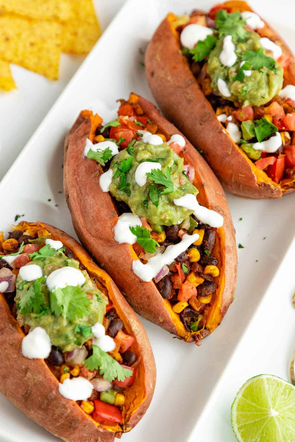 three mexican stuffed sweet potatoes with black beans, corn, guacamole, pico de gallo, and vegan sour cream