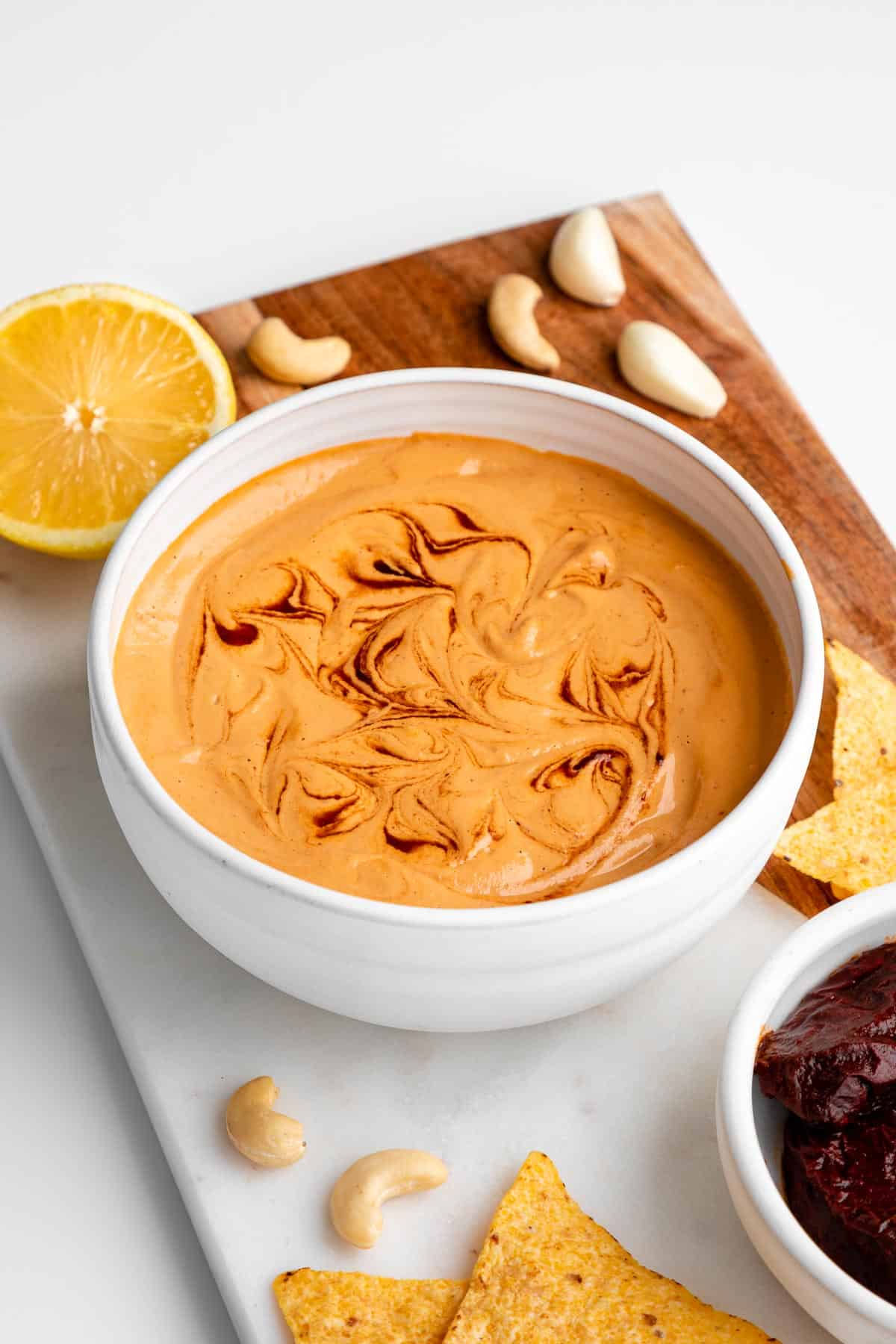 a white bowl filled with vegan chipotle aioli, surrounded by tortilla chips, cashews, lemon, and peppers