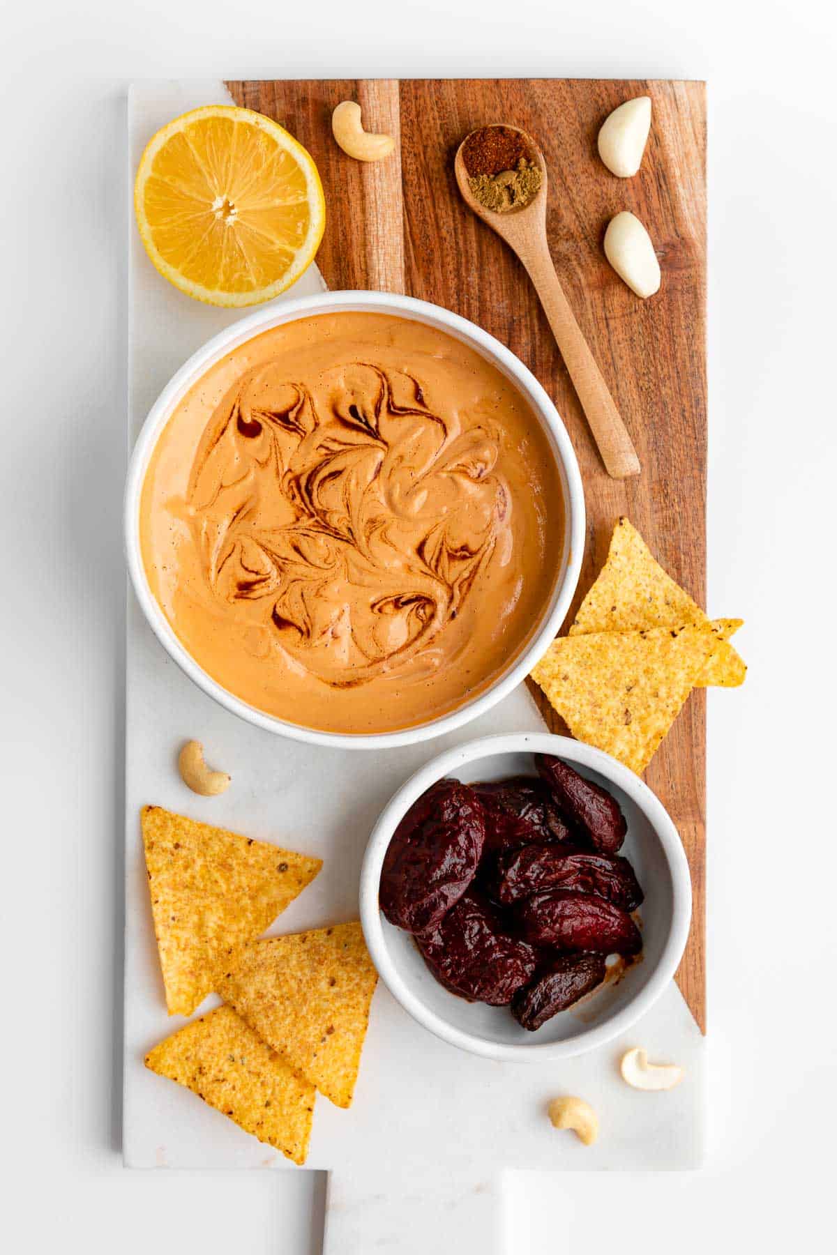 a marble serving board with a bowl of vegan chipotle aioli, tortilla chips, peppers in adobo sauce, lemon, and cashews on top