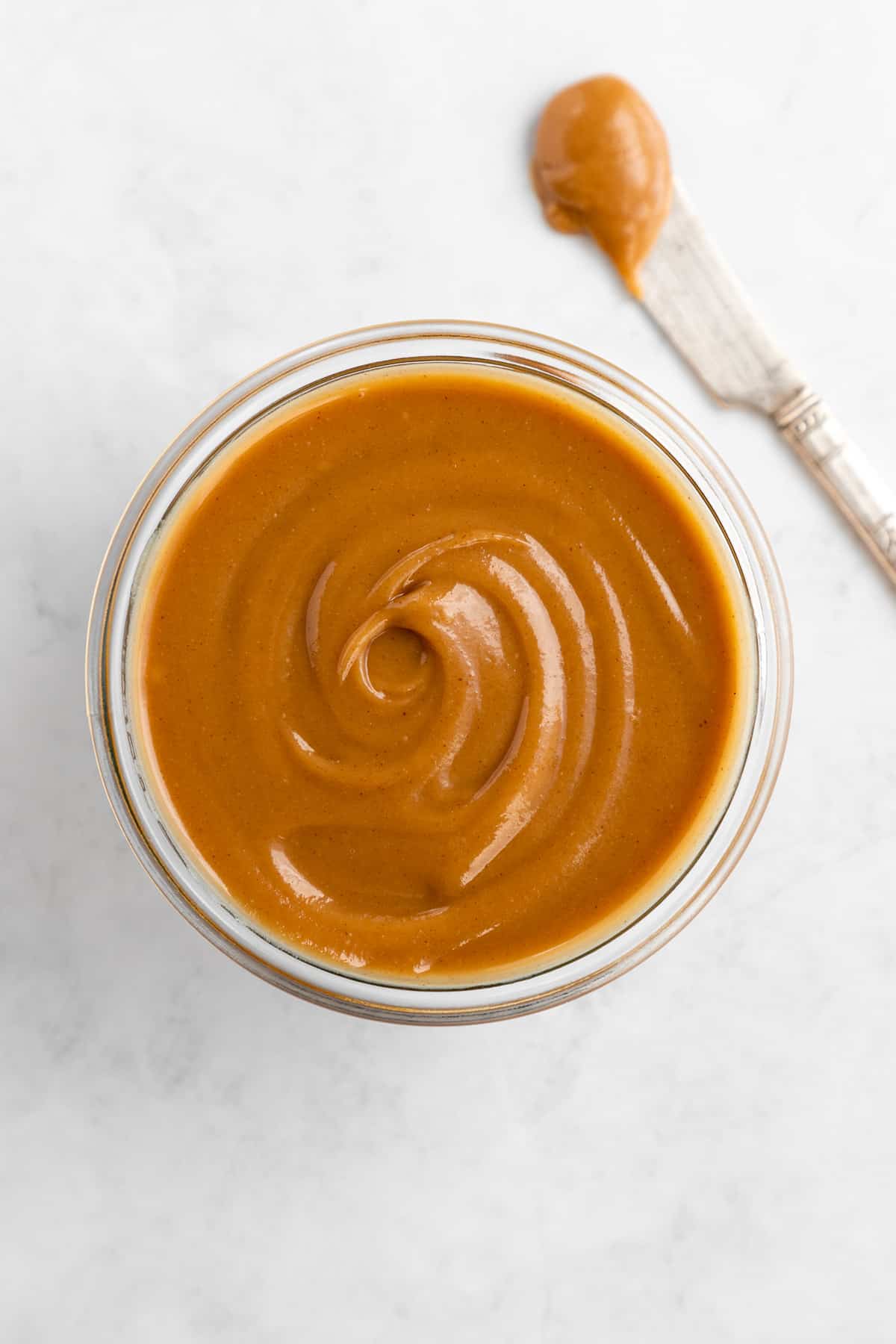 3 ingredient healthy caramel dip swirled inside a glass jar with a knife beside it