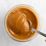 overhead image of a spoon scooping vegan peanut butter caramel out of a glass jar