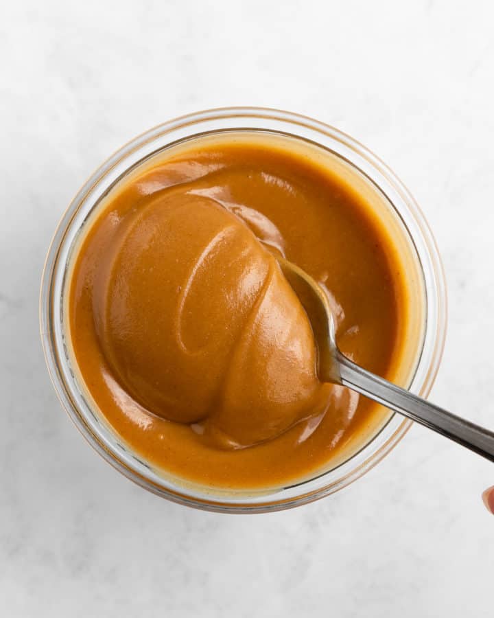 overhead image of a spoon scooping vegan peanut butter caramel out of a glass jar