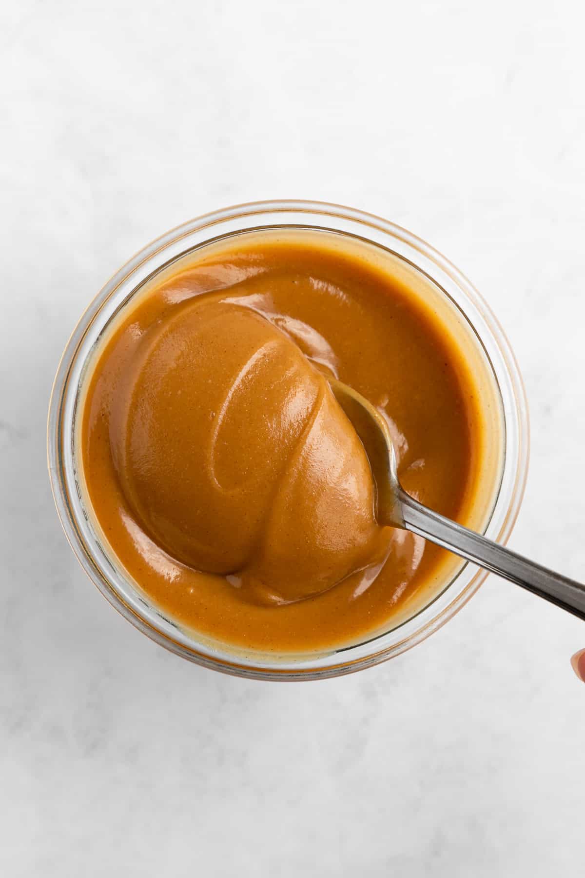 overhead image of a spoon scooping vegan peanut butter caramel out of a glass jar