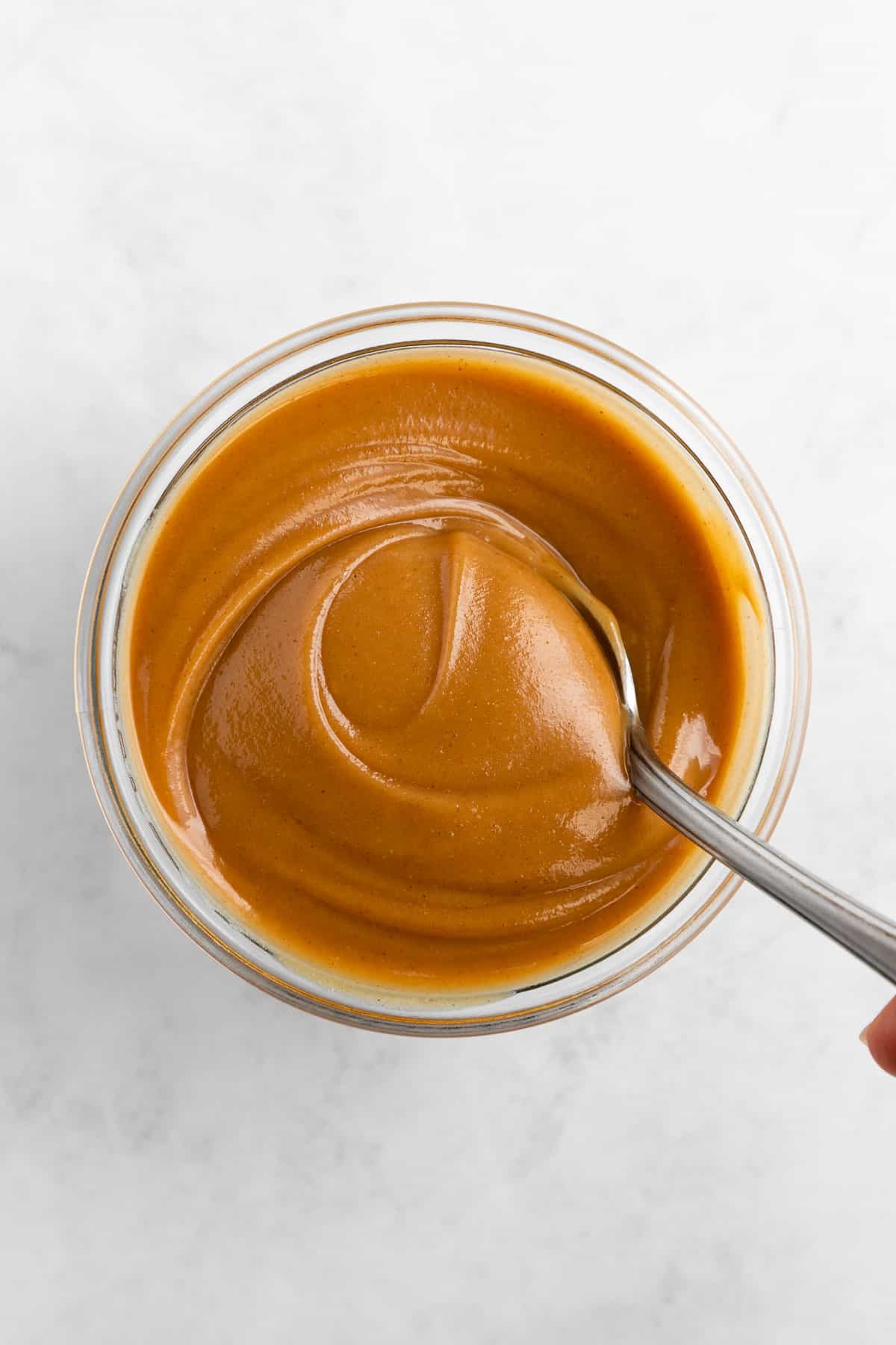 overhead image of a spoon scooping vegan peanut butter caramel out of a glass jar