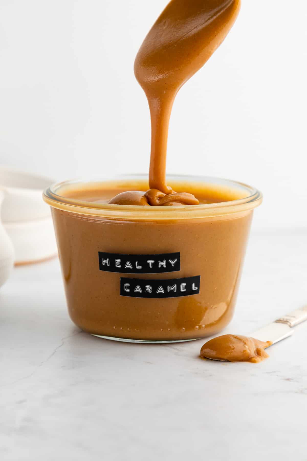 a spoon drizzling vegan peanut butter caramel sauce into a glass weck jar