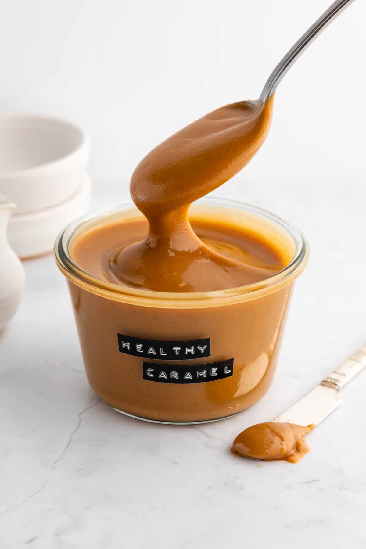 a spoon scooping healthy vegan peanut butter caramel sauce out of a glass weck jar