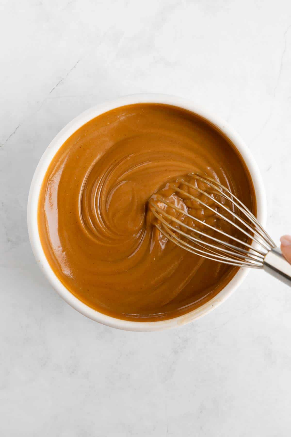 whisking healthy caramel sauce in a white bowl