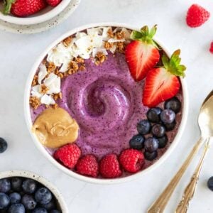 a berry smoothie bowl surrounded by bowls of strawberries, raspberries, and blueberries