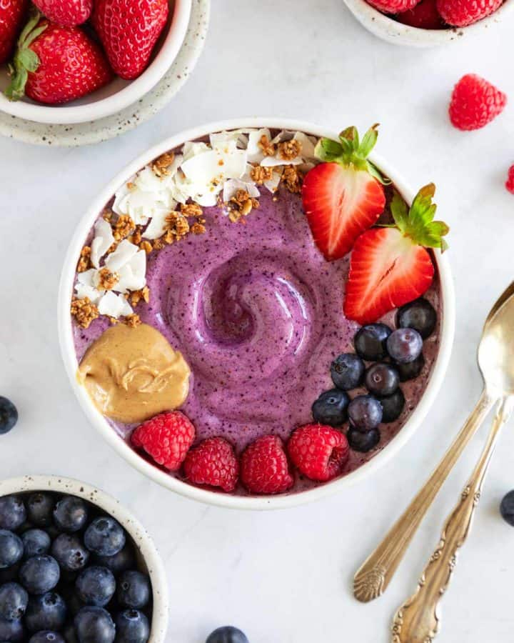 a berry smoothie bowl surrounded by bowls of strawberries, raspberries, and blueberries