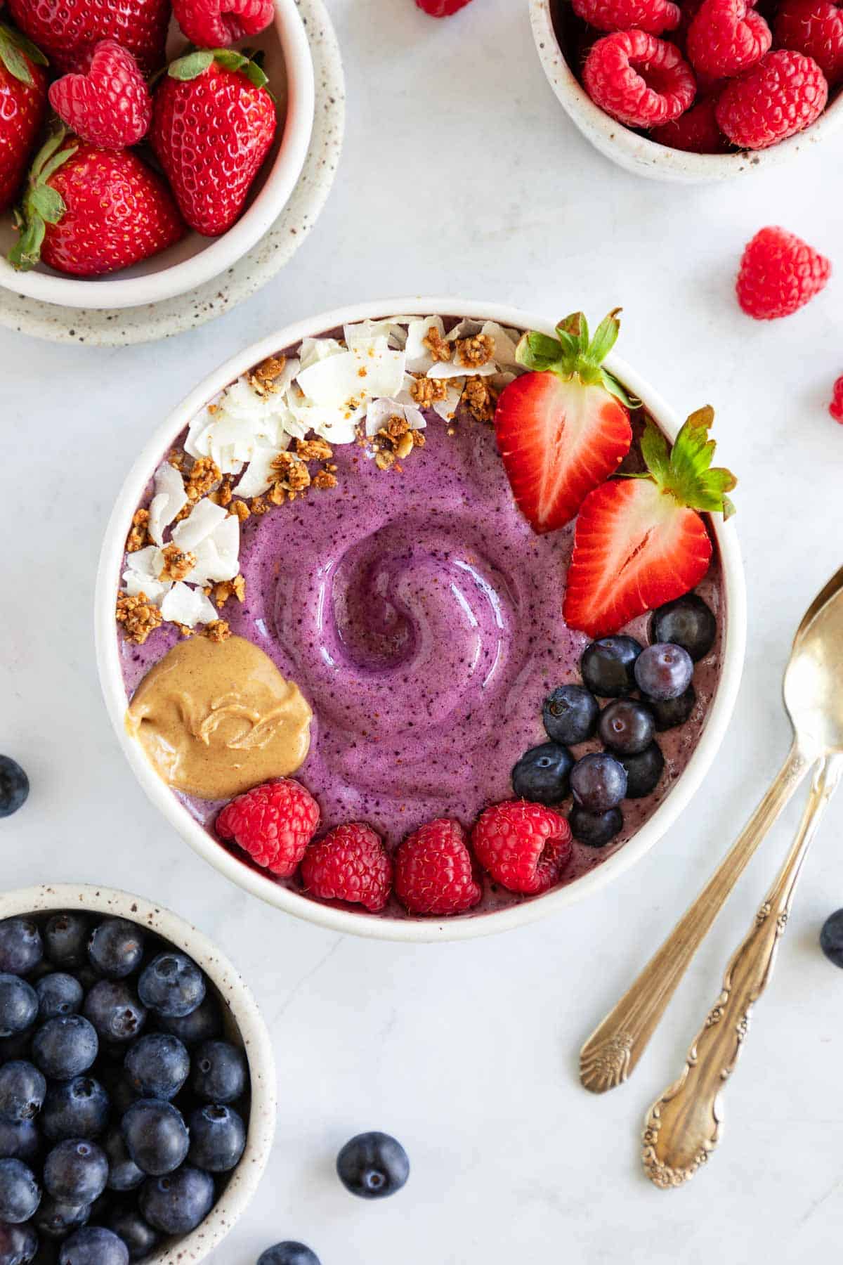 a berry smoothie bowl surrounded by bowls of strawberries, raspberries, and blueberries